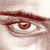 A pixelated close-up of a human eye with a brown iris and dark pupil, set against a light beige background with subtle shading.