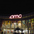 Pixelated image showing a pinkish 'AMC' text logo above a blurred background of indistinct shapes and colors.