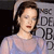 A pixelated static image shows a person with short brown hair wearing a light purple top, standing in front of a gray background with large black letters.