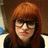 Pixelated portrait of a person with long reddish-brown hair and bangs, wearing dark clothing against a brown background.