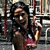 A woman in a sleeveless maroon top holds red poles, smiling with eyes closed against an urban backdrop.