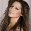A woman with long brown hair and light makeup looks slightly upward against a light background.