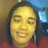 Pixelated static image of a person with dark hair wearing a red top against a blurred background with blue and brown tones.