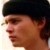 Pixelated profile view of a person wearing a dark cap, light skin tone, and visible ear with earlobe, against a light background.