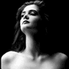 Black-and-white image of a woman with long dark hair, bare shoulders, and closed eyes tilted upward against a black background.