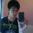 Pixelated image of a person with dark hair wearing a dark jacket over a light shirt, holding a dark rectangular object against a gradient background.