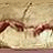 Pixelated image of a figure with brown hair and light skin, wearing a white garment, with a small heart symbol in the bottom right corner.