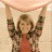 A pixelated figure in a red top and patterned jacket holds a large light-colored object above their head with both arms raised.