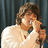 A pixelated image shows a person in a light-colored sweater holding a microphone against a dark curtain, with bold red background and black text reading "I know," "I AM" and "hot!"