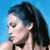 Static pixelated image of a person with long dark hair against a solid blue background, showing partial profile view from shoulder up.