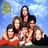 A pixelated group of five people posing together outdoors under a blue sky with green foliage.
