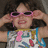 A pixelated image of a person with dark hair wearing pink sunglasses and a colorful patterned shirt with a pink tie, hands raised near the head.