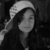 Pixelated grayscale image of a person wearing a light-colored beanie and dark clothing, with long hair partially visible against a dark background.