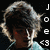 Pixelated image of a person with dark hair and light-colored clothing, featuring vertical white text on the right side against a black background.