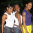 Three people stand side-by-side in a pixelated image; two wear white tank tops and blue jeans, one wears purple shirt and yellow shorts.