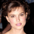 Pixelated close-up of a person with brown hair styled in an updo, light skin tone, and pink lips against a dark background.