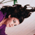 Pixelated image of a person with dark hair lying on a light surface, wearing a purple garment and white top, with a green object visible above.