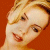 Pixelated close-up of a person's face with light skin and blonde hair against an orange background, showing visible facial features including eyes, nose, mouth, and eyebrows.