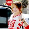 A person in a red and white patterned top stands near a vehicle with a red stop sign visible behind them.