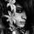 Black-and-white image of a person with dark hair wearing a flower accessory and dark necklace, displayed in a of repeated