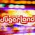 Animated icon with 'SugarLand' text in red outline over a colorful, pixelated background of orange, purple, and green hues.