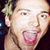 A pixelated image shows a person with light brown hair and an open mouth, next to red and blue text on black background.