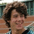 A person with curly brown hair smiles in a of four showing slight variations in head position and background elements