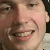 Pixelated close-up of a person's face showing a broad smile with visible teeth, light skin tone, and dark hair on the right side.