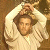 Pixelated static image of a person in light-colored clothing with raised arms against a brown background.