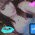 A pixelated image of a person with long dark hair, light skin, and a blue top, featuring cyan rings and pink heart shapes in the background.