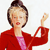 Pixelated image of a person with short dark hair wearing a red jacket over a pink top, raising their right hand in a gesture.