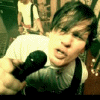 A person in a white shirt and dark suspenders holds a black microphone, with background figures visible; the image shifts through motion blur effects across frames.