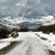 Pixelated landscape with layered horizontal bands of blue sky, white clouds, dark brown terrain, and light gray ground, rendered in low-resolution blocky style.