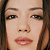 Pixelated close-up of a person's face with brown hair, visible eyes, nose, and lips on a transparent background.