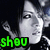 Pixelated grayscale image of a person with short dark hair, wearing a dark top, making a hand gesture near their face, with green text 'shou' in the bottom-left corner.