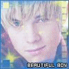 Pixelated close-up of a person with light hair and blue eyes, wearing a dark shirt with yellow stars, under bright lighting.