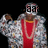 A person in a red shirt and patterned jacket with multiple necklaces, holding up one hand against a black background.