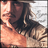 A close-up of a person with long wavy hair wearing a light brown jacket and a wide-brimmed hat, hand resting near the chin.
