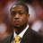 A pixelated static image shows a person in formal attire with dark hair, wearing a white collared shirt and yellow tie under a dark jacket against a blurred background.