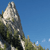 A pixelated image shows a tall, rocky mountain peak with green vegetation on its slopes against a clear blue sky.