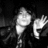 Pixelated grayscale image of a figure with a rounded head and body, one arm raised in a waving gesture, against a dark background.