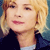 Pixelated close-up of a person with blonde hair wearing a dark jacket over a light shirt against a blue background.