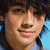 A person with dark tousled hair and light skin wears a blue shirt against a bright blue background, shown in four