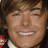 Pixelated close-up of a smiling person with brown hair, visible teeth, and a white collar, set against a dark background with red and white elements.