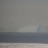 A static image showing a gradient sky above a calm sea with a sandy shore, rendered in muted tones of gray, blue, and beige.