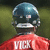 Pixelated image of a figure wearing a blue helmet and red shirt with white text, set against a green background.