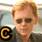 A pixelated image of a person with light brown hair and sunglasses, wearing a dark shirt against a blurred background.