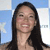 A pixelated portrait of a person with long dark hair, light skin, and a smiling expression against a blue and white background.