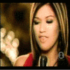 A woman with long brown hair and red shoulderless top sings into a microphone, her mouth and facial expressions changing across frames.
