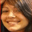 Pixelated close-up of a smiling person with light brown hair and warm skin tones against a dark background.